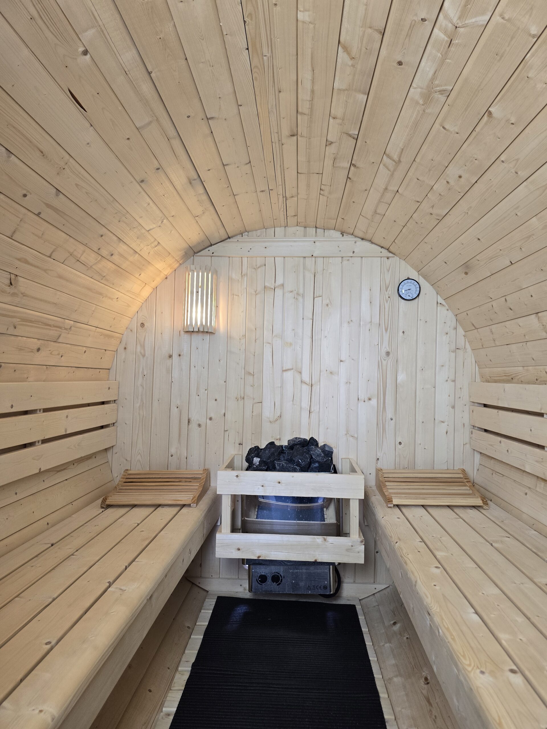 Innenraum der FrankenFass Fasssauna mit Holzbänken, Saunaofen und Thermometer