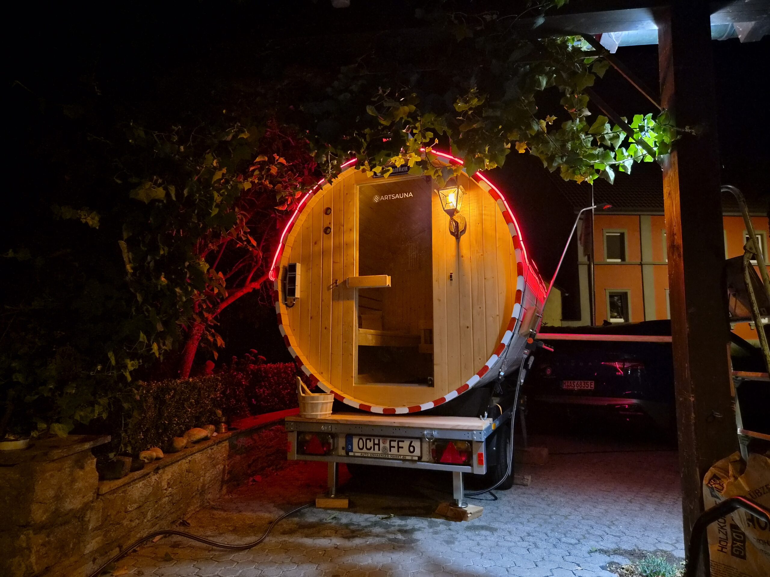 Mobile FrankenFass Fasssauna bei Nacht, Blick durch die offene Tür ins beleuchtete Innere